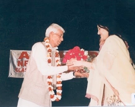 Man receiving flower garland on stage at cultural event