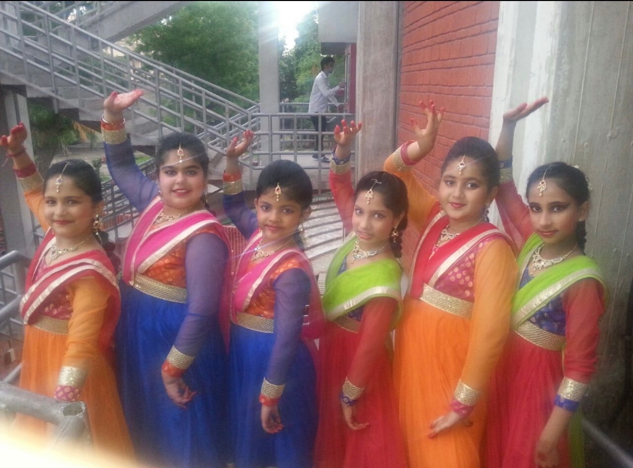 Seven young students in colorful traditional costumes backstage