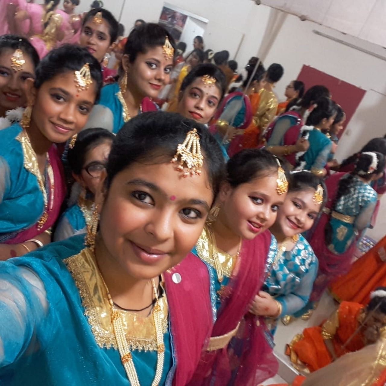 Students in teal and gold dance costumes taking a backstage selfie before performance