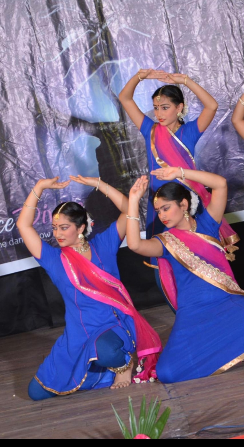 Three dancers in blue and pink costumes performing on stage
