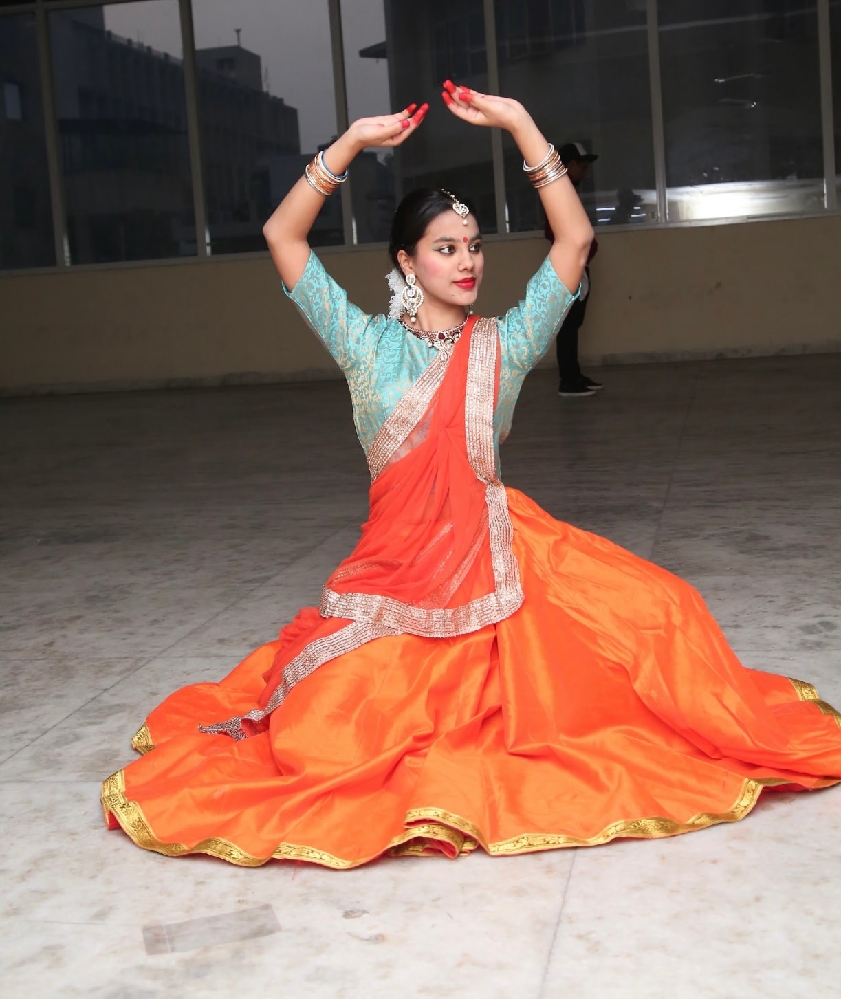 Dancer in orange lehenga in graceful seated Kathak pose