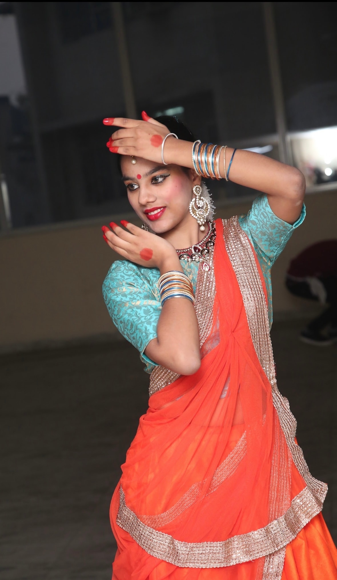 Student in orange and teal saree performing expressive Kathak mudra